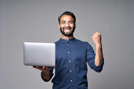 191500072 happy indian business man holding laptop isolated on gray celebrating result